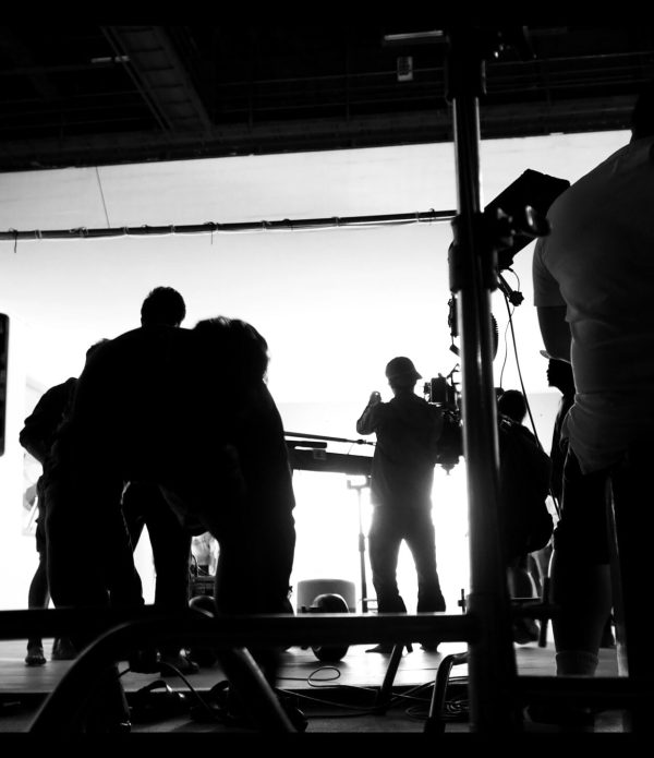 Behind the shooting video production and lighting set for filming which movie crew team working and silhouette shadow of camera and professional equipment in big studio for commercial advertising.